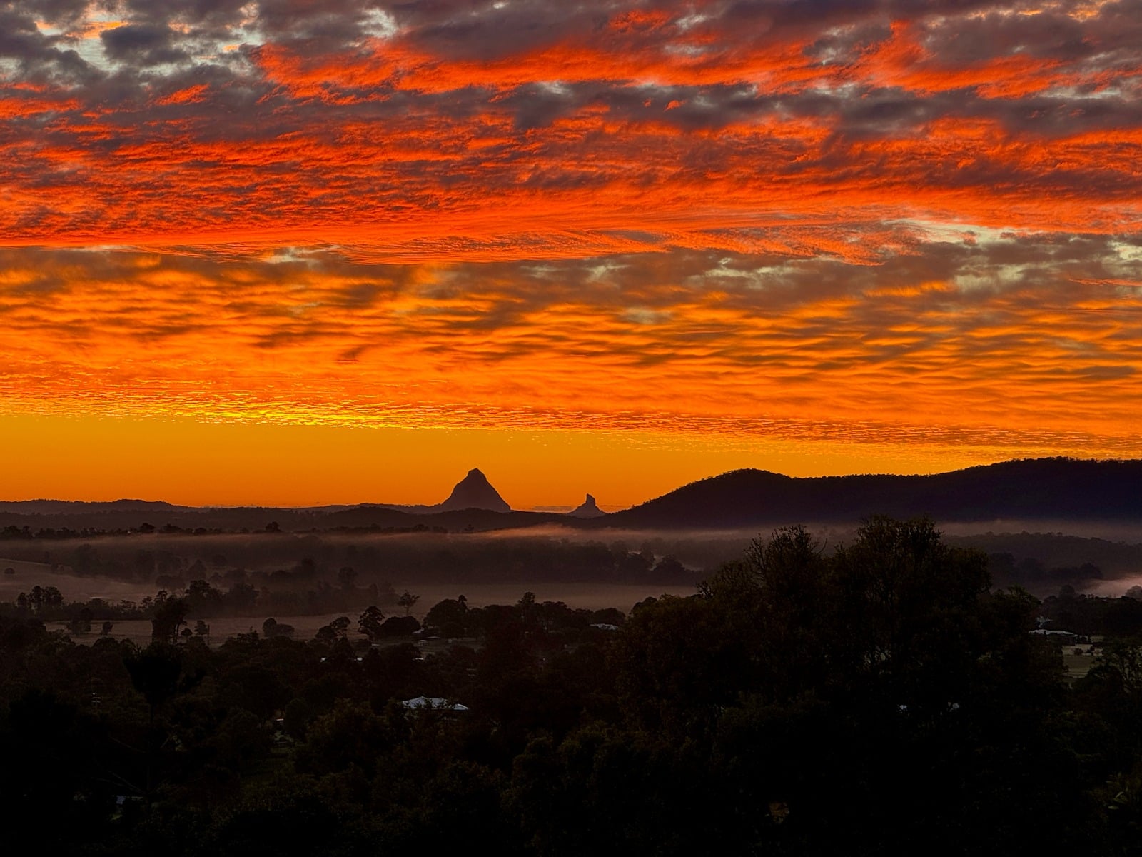 Fiery sunrise over the Glass House Mountains with morning mist in the valley